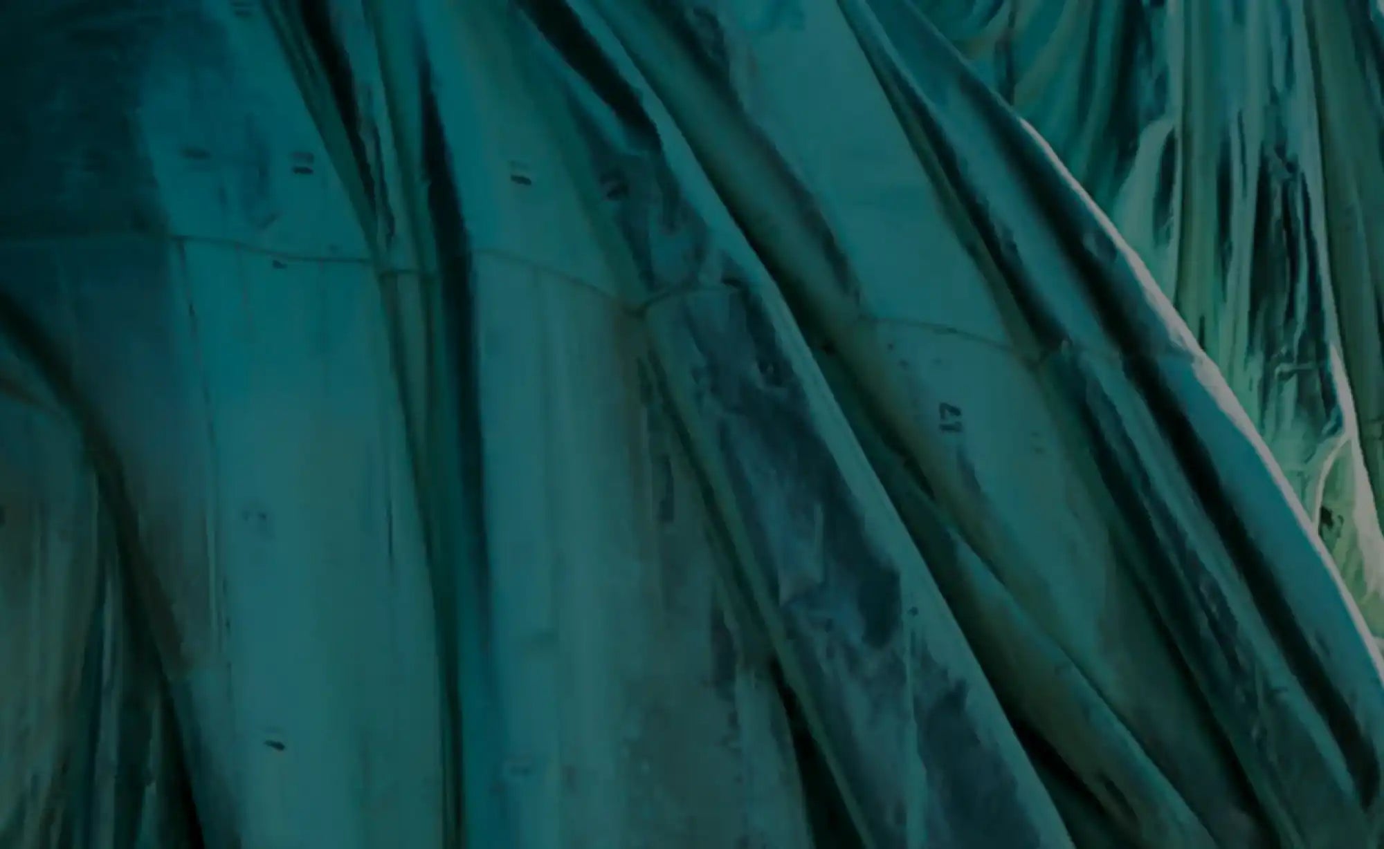 Flowing fabric or material in deep teal tones with diagonal draping folds.